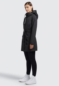 Musta vedenpitävä parka, jossa on säädettävä huppu ja kiristettävä vyötärö. Siinä on kaksi sivutaskua ja logotyyppinen yksityiskohta. Yhdistetty mustiin legginsseihin ja valkoisiin tennareihin.