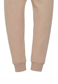 Pantaloni della tuta beige realizzati in tessuto morbido, con gambe affusolate e polsini a coste alle caviglie per comfort e una vestibilità aderente.