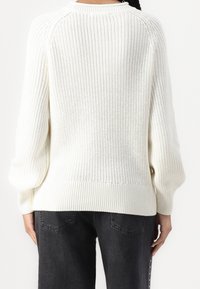 Pull en ivoire en maille avec un motif à points texturés, manches raglan et ourlet côtelé. Le dos présente une coupe ample et un style de manches ballon.