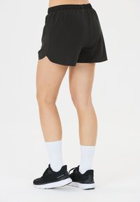 Schwarze Sportshorts mit elastischem Bund und abgerundetem Saum. Kombiniert mit schwarzen Turnschuhen und weißen Crew-Socken vor einem schlichten Hintergrund.