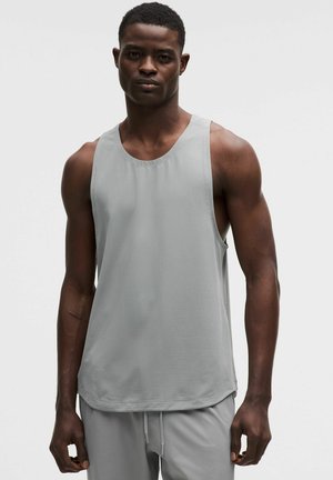 Homme aux cheveux courts portant un débardeur sportif gris clair et un short assorti sur un fond uni