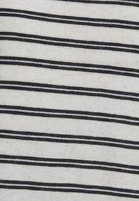 Biały materiał z równomiernie rozmieszczonymi poziomymi czarnymi paskami, ukazujący dzianinową fakturę i drobne detale.