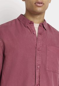 Camicia rosa con bottoni, in un tessuto morbido con una finitura testurizzata, dotata di una tasca sul petto e di un colletto classico.