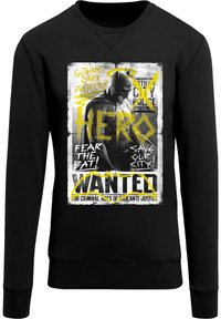 Sudadera negra con un diseño gráfico de un vigilante temático de murciélago. La impresión incluye texto amarillo y una textura desgastada, similar a un cartel.