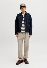 Σκούρο τζιν μπουφάν με κούμπωμα με κουμπιά και τσέπες στο στήθος, λευκό και ναυτικό μπλουζάκι με ρίγες, μπεζ παντελόνι, καφέ παπούτσια και ελιά καπέλο.