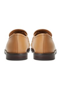 Tan leren schoenen met een afgeronde vorm, subtiele stikdetails en een lage bruine hak, gezien vanaf de achterkant tegen een witte achtergrond.
