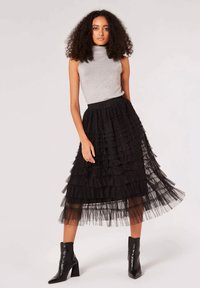 Jupe en tulle noire avec des volants superposés, associée à un top sans manches argenté. Elle présente une taille cintrée et une coupe à mi-genoux. Bottes à talons noires.