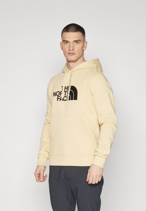 Beige hoodie lavet af bomuldsblanding, med en frontlomme, justerbar snorhætte og sort logo print på brystet.