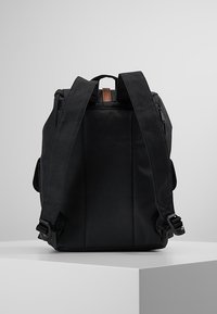 Zwarte rugzak met verstelbare riemen, gemaakt van gestructureerde stof. Voorzien van een handvat bovenaan en een rits aan de zijkant. Eenvoudig, gestructureerd ontwerp.