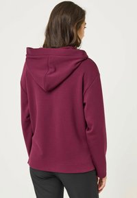 Bordeauxkleurige hoodie met een grote achterkap, losse pasvorm en zachte textuur. Het ontwerp heeft een rechte zoom en geribde manchetten.
