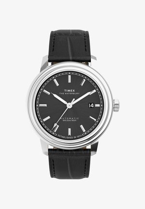 Automatické hodinky Timex Waterbury so strieborným púzdrom, čiernym koženým remienkom s textúrou, tmavosivým ciferníkom a okienkom na dátum o tretej hodine.