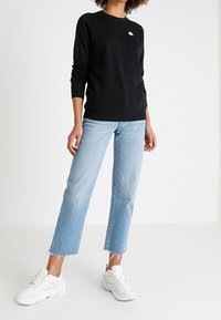 Svart sweatshirt med långa ärmar och rund halsringning. Ljusblå rakbenade jeans med fransade fållar. Vita sneakers fulländar looken.