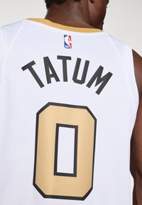 Witte basketbaltruit met een gouden en zwarte nummer "0" en de naam "TATUM" in zwarte letters erboven. NBA-logo op de nek.