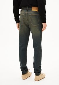 Denimjeans in donkergroen met een vervaagd effect. Voorzien van twee achterzakken en een bruine leren labelpatch. Slim fit met taps toelopende benen.