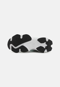 Sål av en sneaker med svarte teksturerte gripputer på en hvit base og en "STIL" logo preget i midten under buen.