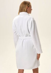 Biała, polarowa szlafrok z kołnierzem szalowym, z paskiem w talii i fakturowanymi mankietami. Miękki materiał i średnia długość zapewniające komfort.