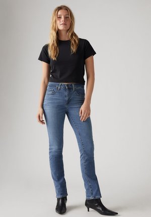 T-shirt cropped noir associé à un jean droit bleu clair et des bottines noires. Les jeans disposent de poches avant et d'une finition en denim classique.