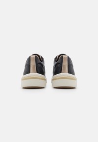Black shoes with a smooth leather finish, a beige synthetic heel accent, and a white midsole, featuring a textured pattern on the upper.