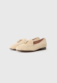 Beige suede loafers with a rounded toe, decorative bow detail, and a small, stacked heel. Smooth texture and simple design.