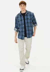 Blå og sort ternet flannel skjorte med knapper, oprullede ærmer, parret med lyse beige bukser og hvide sneakers.