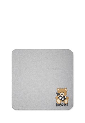 Tappeto in cotone grigio con una grafica di un orso che tiene un giocattolo, con la scritta "MOSCHINO" in caratteri in grassetto vicino ai piedi dell'orso.