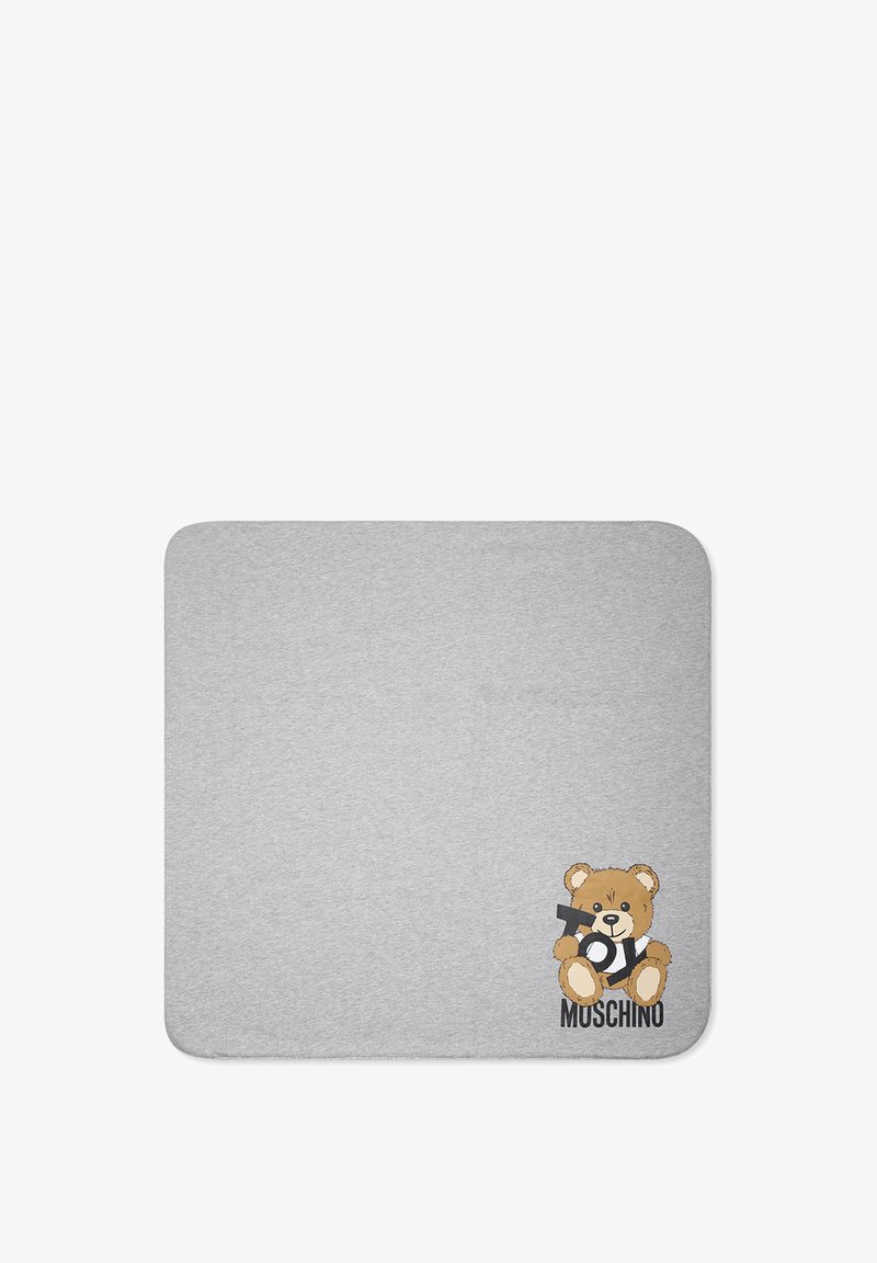 Tappeto in cotone grigio con una grafica di un orso che tiene un giocattolo, con la scritta "MOSCHINO" in caratteri in grassetto vicino ai piedi dell'orso.