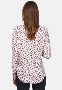Langarmshirt met een witte basis en een rood bloemenpatroon. Zacht fabric, gebogen zoom, met knopen afgesloten mouwen en een getailleerd silhouet.