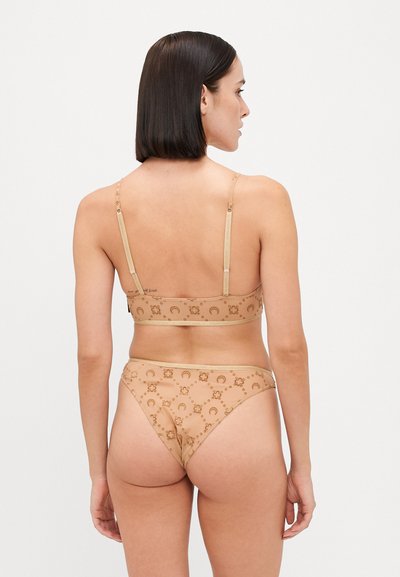 Beige lingerie set featuring a sheer bralette and matching thong with circular patterns and adjustable straps. Soft texture and lightweight design.