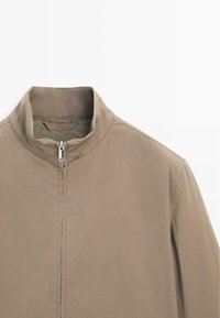 Beige letvægtsjakke med opretstående krave, lynlås foran og glat tekstur. Har rene linjer og et minimalistisk design.