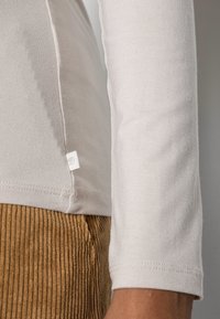 Vaaleanharmaa pitkähiha paita, jossa on istuva malli, pehmeä pinta ja tikatut saumat, yhdistettynä ruskeisiin ribbineulottuihin samettihousuihin.