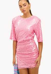 Robe à paillettes roses avec des manches courtes et un design froncé, dotée d'un col rond et d'une texture lisse. Accessoirisée avec un sac multicolore.