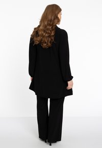 Sort tunika med lange ærmer og løst fit, parret med sorte brede bukser, glat tekstur, minimalistisk design.
