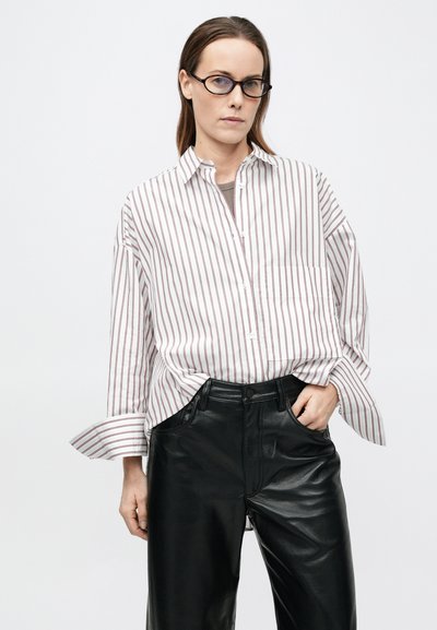 Triibuline nööpidega särk, millel on punased ja valged vertikaalsed triibud; lõdva lõikega, pikkade varrukatega ja ühe rinnataskuga. Sobitatuna mustade nahksete pükstega.