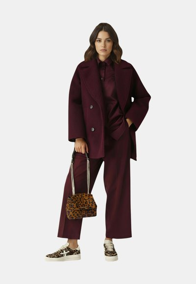 Cappotto doppiopetto color bordeaux con colletto oversize, abbinato a camicia e pantaloni bordeaux, completato da sneakers e borsa con stampa leopardata.
