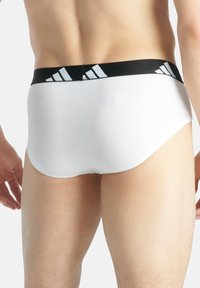 Weiße Herrenunterhosen mit einem schwarzen elastischen Bund und einem hellblauen Logo-Muster. Der Stoff wirkt glatt und dehnbar.