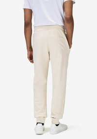 Beige joggers med snörning i midjan, elastiska muddar och en enda bakficka, matchat med vita sneakers och en enkel vit t-shirt.