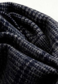 Tela de patrón azul marino y gris, lana texturizada con una apariencia suave y aterciopelada, mostrando un diseño de pata de gallo en una disposición doblada.