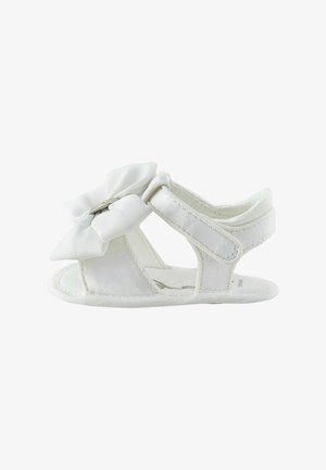 Sandalo bianco per bambino con un grande fiocco di stoffa sulla parte anteriore, design con punta aperta e cinturino regolabile alla caviglia.