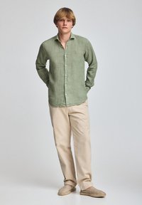 Camicia in lino verde chiaro con chiusura a bottoni, abbinata a pantaloni di cotone beige e espadrillas marroni. Design semplice e vestibilità rilassata.