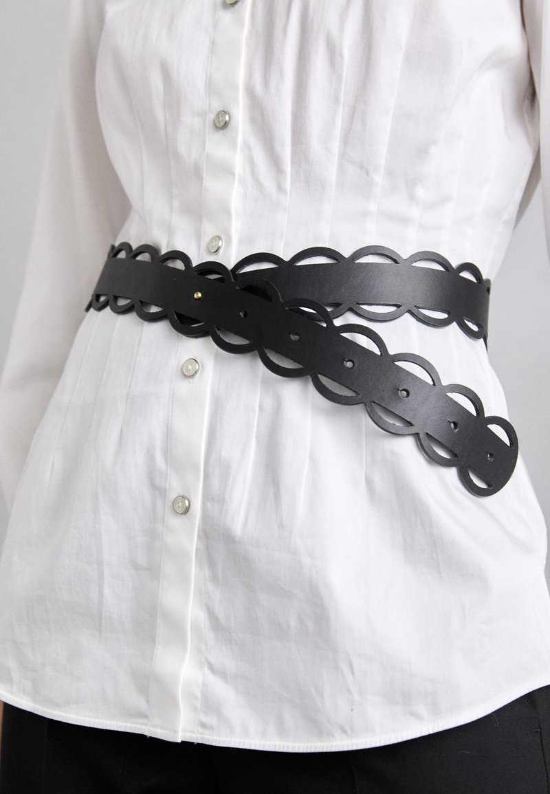 Black leather belt with circular cutouts and a smooth texture, featuring a decorative wave pattern and a single golden stud accent.