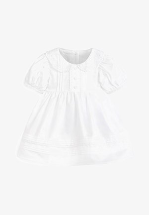Robe blanche pour bébé avec manches ballon, col Peter Pan bordé de dentelle, devant boutonné, et plis décoratifs sur la jupe et le corsage.