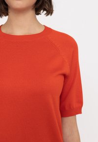 Czerwony, dziergany sweter z krótkim rękawem, z okrągłym dekoltem oraz prążkowanymi akcentami na rękawach i dolnym hemie, o gładkiej fakturze przez cały czas.