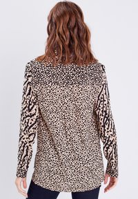 Blouse à manches longues en tissu beige avec des motifs animaux et géométriques noirs, ourlet arrondi et coupe décontractée.