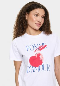 Balta medvilninė marškinėlių su dideliu raudonos vyšnios grafiniu dizainu ir mėlynu tekstu "POMME D'AMOUR", apvaliu iškirpimu, trumpomis rankovėmis.