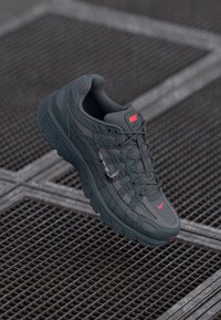 Dark grey sneaker with textured fabric, a reinforced toe cap, breathable mesh panels, and red accents on the logo and sole.