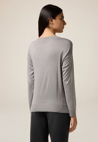 Grauer Pullover mit langen Ärmeln, der strukturierte Akzente und kleine dekorative Nieten an den Ärmeln aufweist. Weicher Stoff mit einer entspannten Passform.