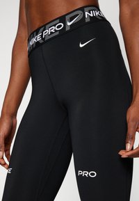 Leggings neri elasticizzati con un elastico brandizzato. Presentano un design aderente, cuciture piatte e testo bianco con la scritta "PRO" e il logo Nike.