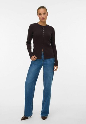 Cardigan côtelé marron foncé avec un col rond et une fermeture à boutons, associé à un jean en denim bleu à jambe large.