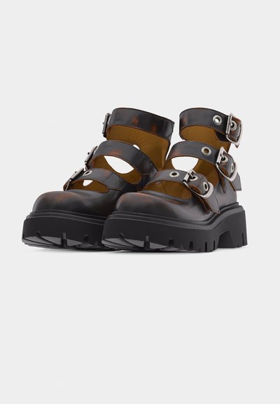 Χοντρά μαύρα δερμάτινα μποτάκια με τρεις ρυθμιζόμενες αγκράφες και παχιά σόλα με ανάγλυφο, τοποθετημένα πλάι πλάι σε λευκό φόντο.