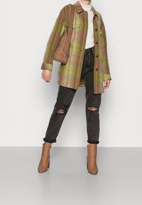 Grønt og brunt ternet oversized jakke, hvid turtleneck, slidte sorte jeans og brune hælankelstøvler, med en brun skuldertaske.
